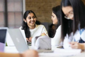 Three female students chatting and laughing whilst working on their laptops