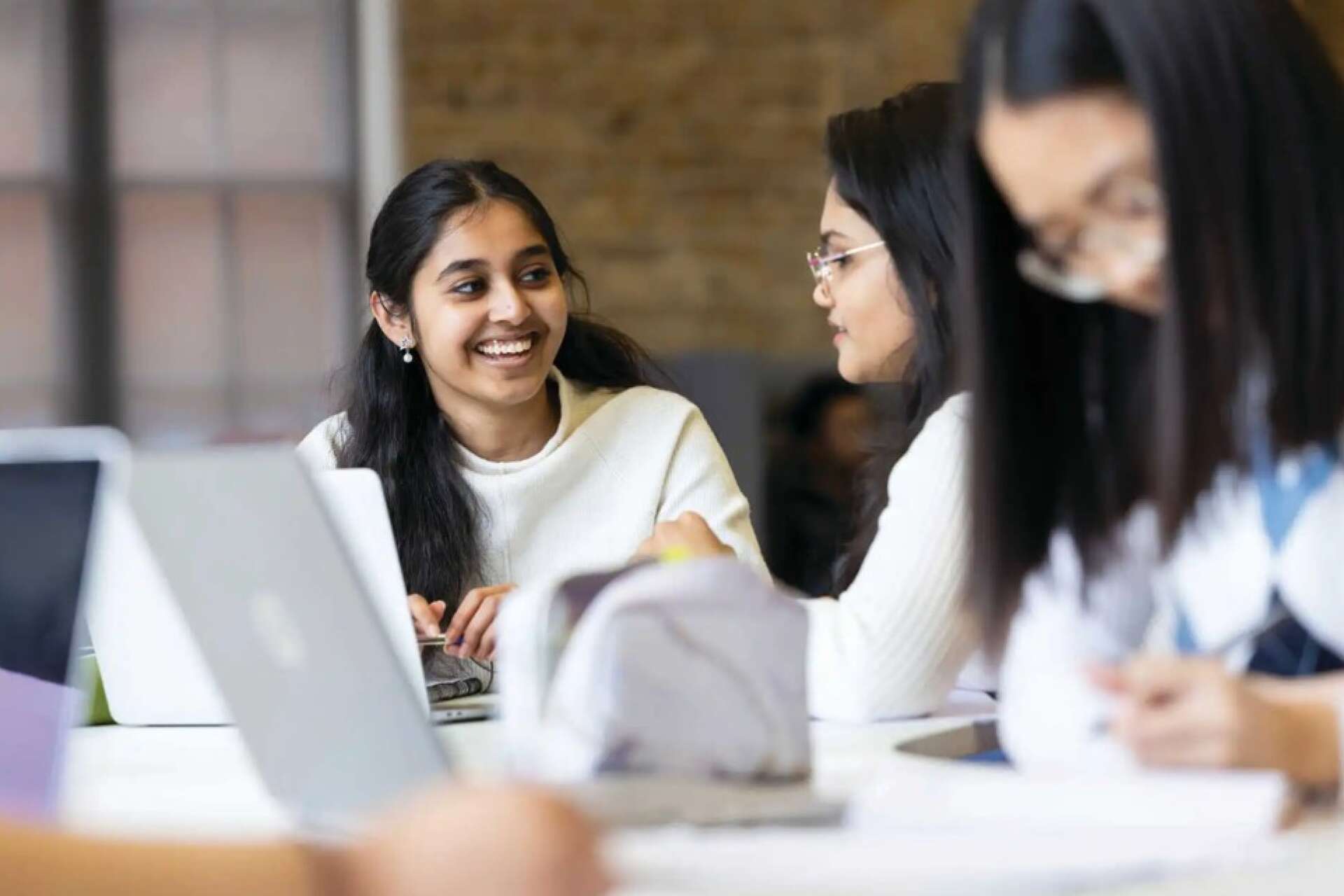 Three women laughing and chatting using laptops